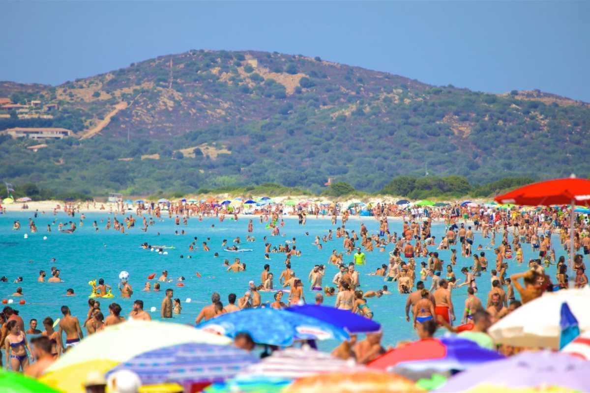 Bambini giocano sulla spiaggia di La Cinta a San Teodoro, atmosfera rilassata, genitori sorridenti, mare cristallino, giochi in sabbia